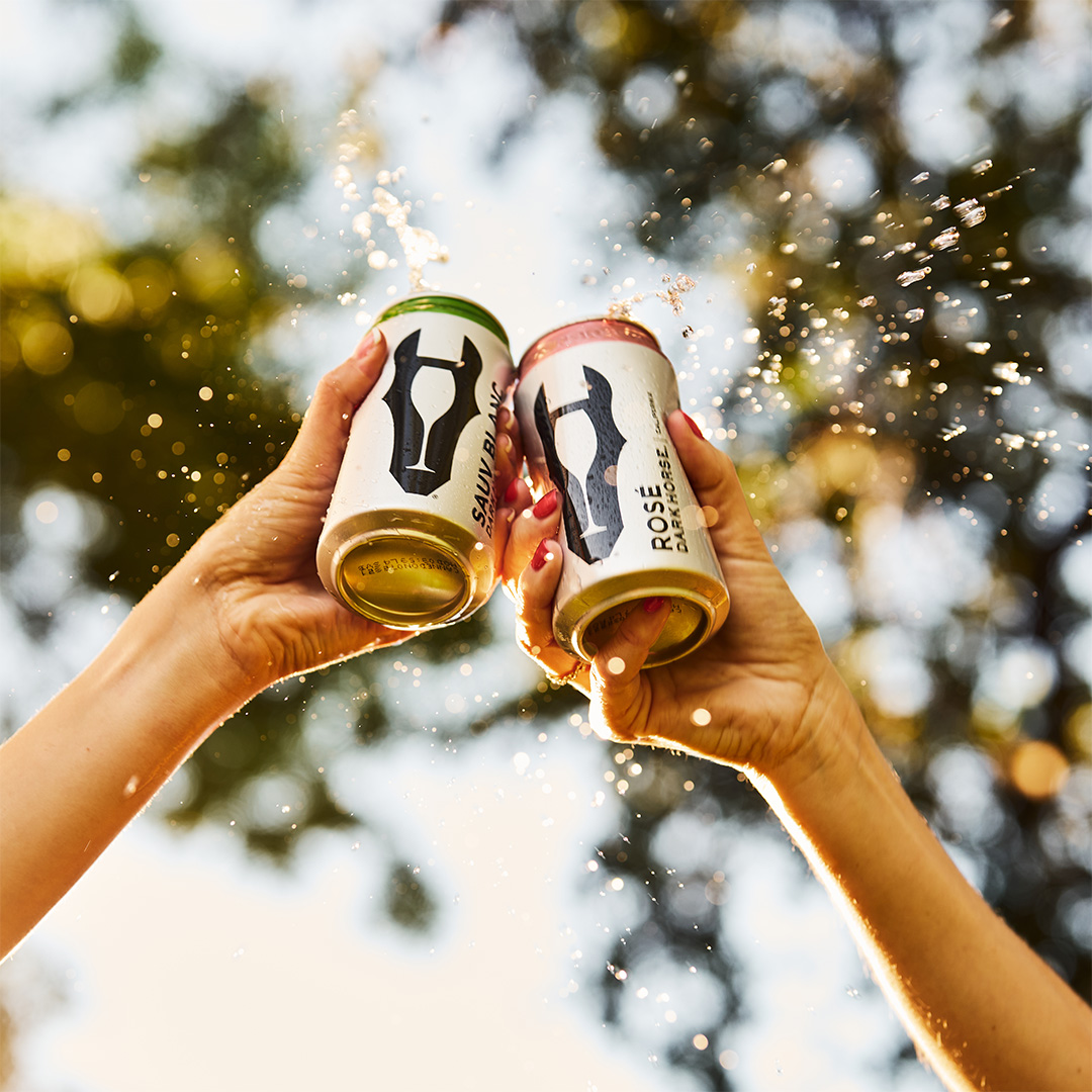 two hands cheersing with Dark Horse cans